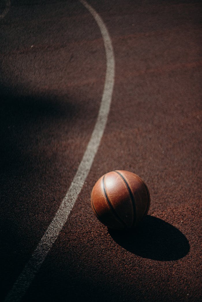 A basketball resting on an outdoor court, casting a shadow under warm daylight.